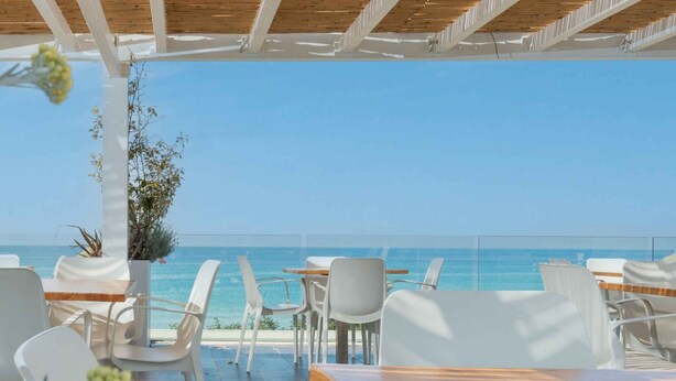 Ein Außenbereich mit weißen Stühlen und Tischen mit Blick auf das Meer.