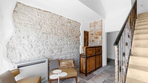 Una habitación con pared de piedra, un armario de madera, un banco y una escalera.