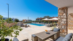 Un espace aménagé au bord de la piscine, avec des chaises longues, une table en bois et des murs en pierre.