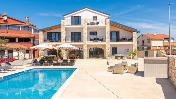 Un edificio de dos pisos con piscina, mobiliario exterior y fachada de piedra.