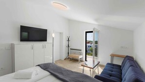 Una habitación de hotel moderna con cama, televisor, escritorio, silla, sofá y balcón con vistas.