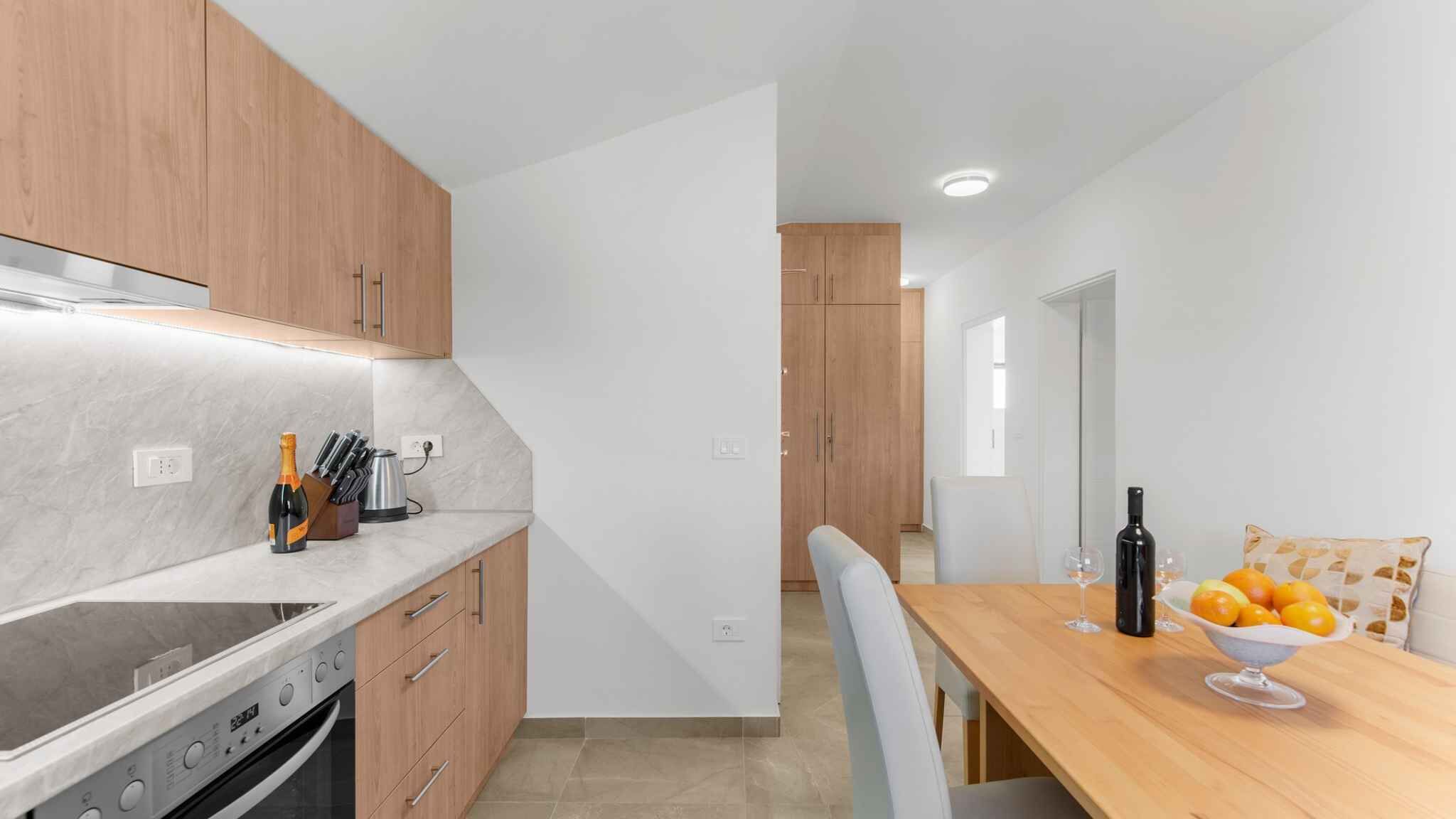 A modern kitchen with wooden cabinets, a marble countertop, and a dining area with a wooden table and chairs.