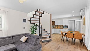 Een moderne woonkamer met een grijze bank, een houten trap en een eethoek met oranje stoelen.