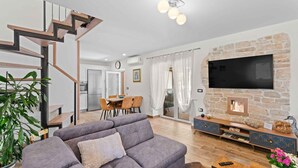 Een moderne woonkamer met een grijze bank, een houten trap, een stenen open haard en een flatscreen televisie die aan de muur is bevestigd.