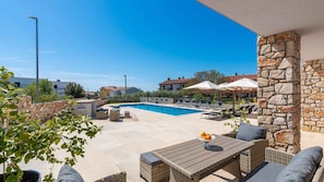 A poolside area with lounge chairs, a table, and a stone wall.