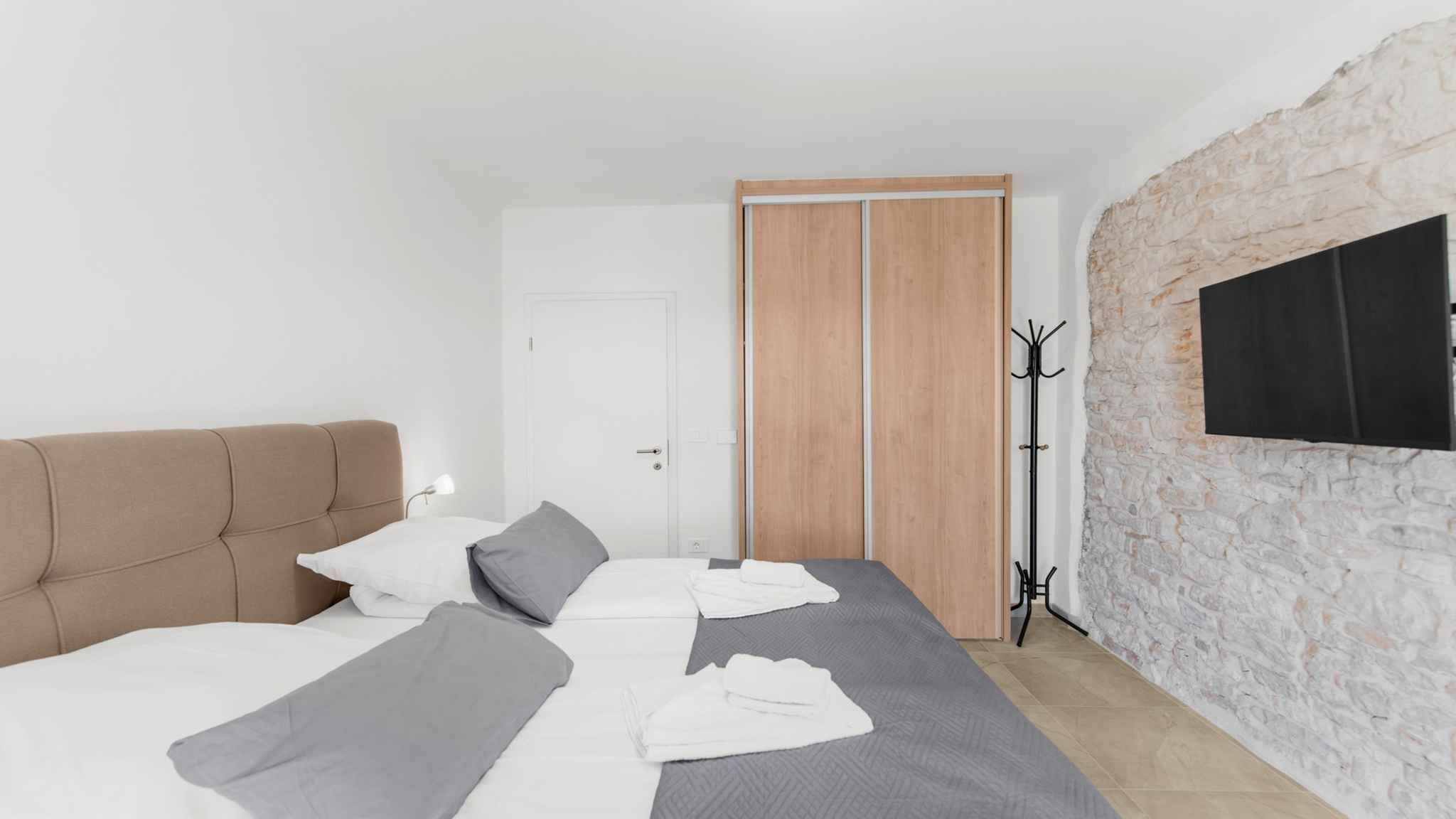Ein Schlafzimmer mit Bett, Kleiderständer, Schrank und Steinwand.