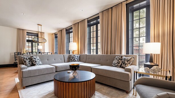 A modern living room with a sectional sofa, a round coffee table, and large windows with curtains.