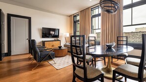 A modern dining area with a round table, six chairs, and a television mounted on the wall. - 2BR Vibrant Stay Steps to French Quarter | The Mayfair (New Orleans)