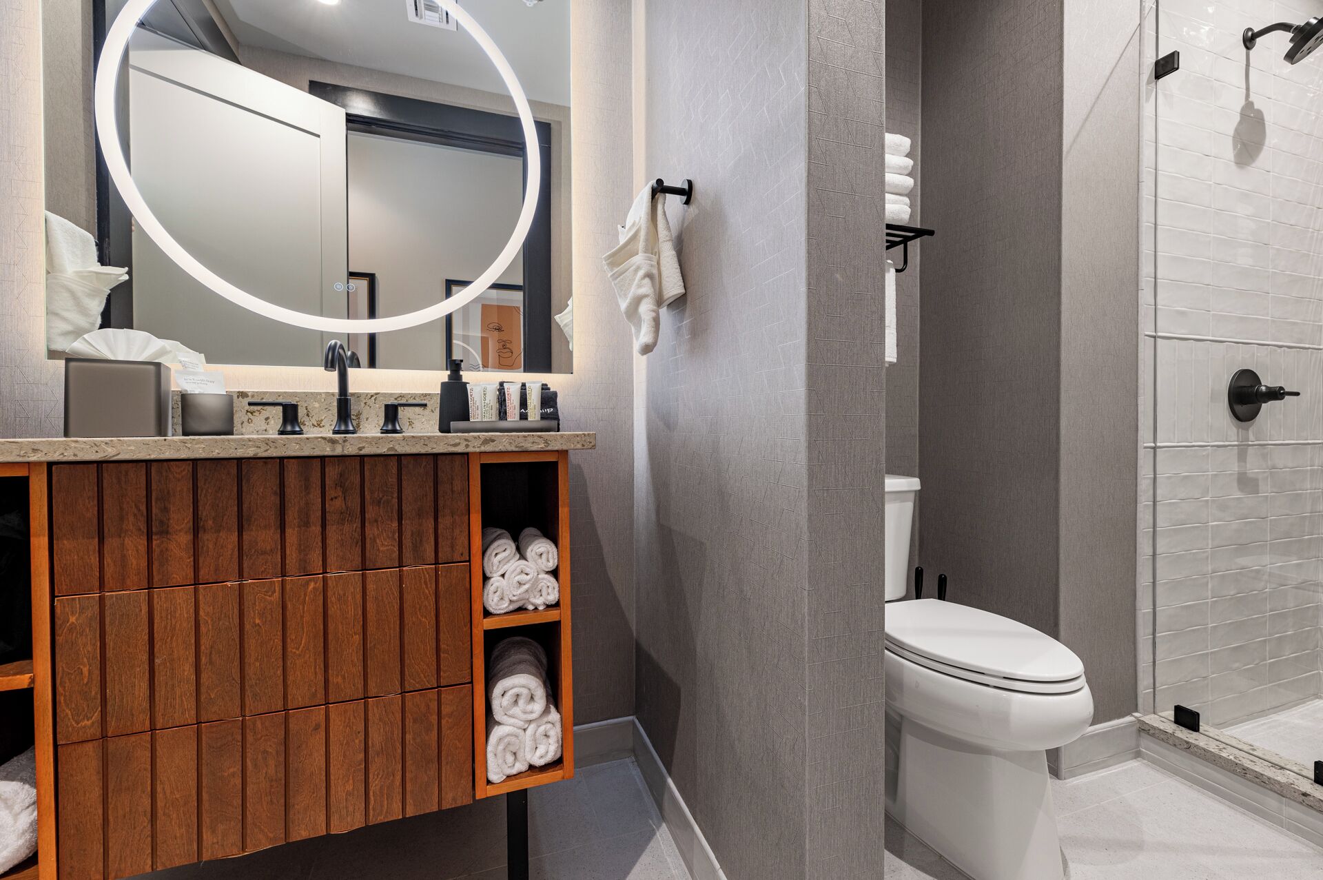 Un baño moderno con tocador de madera, un espejo grande, inodoro y zona de ducha.