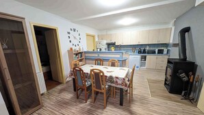 A compact kitchen with wooden cabinets, a dining table with chairs, a clock on the wall, and a wood-burning stove. - Holiday home with wifi and air conditioning (Ságvár)