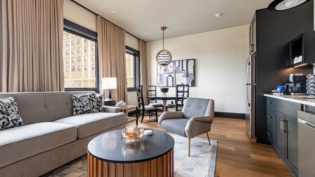 A modern living room with a sofa, armchair, coffee table, and dining area. - 1BR Penthouse Steps to French Quarter | The Mayfair (New Orleans)