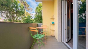 Ein Balkon mit Tisch und Stühlen, einer kleinen Ablage und einer Schiebetür zu einem Innenraum.