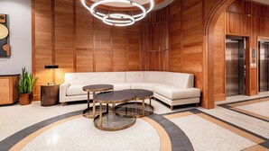 A modern lobby with a white sofa, two round tables, a unique circular light fixture, and a wooden panel wall. - 3BR Charming Stay Walk to French Quarter | The Mayfair (New Orleans)