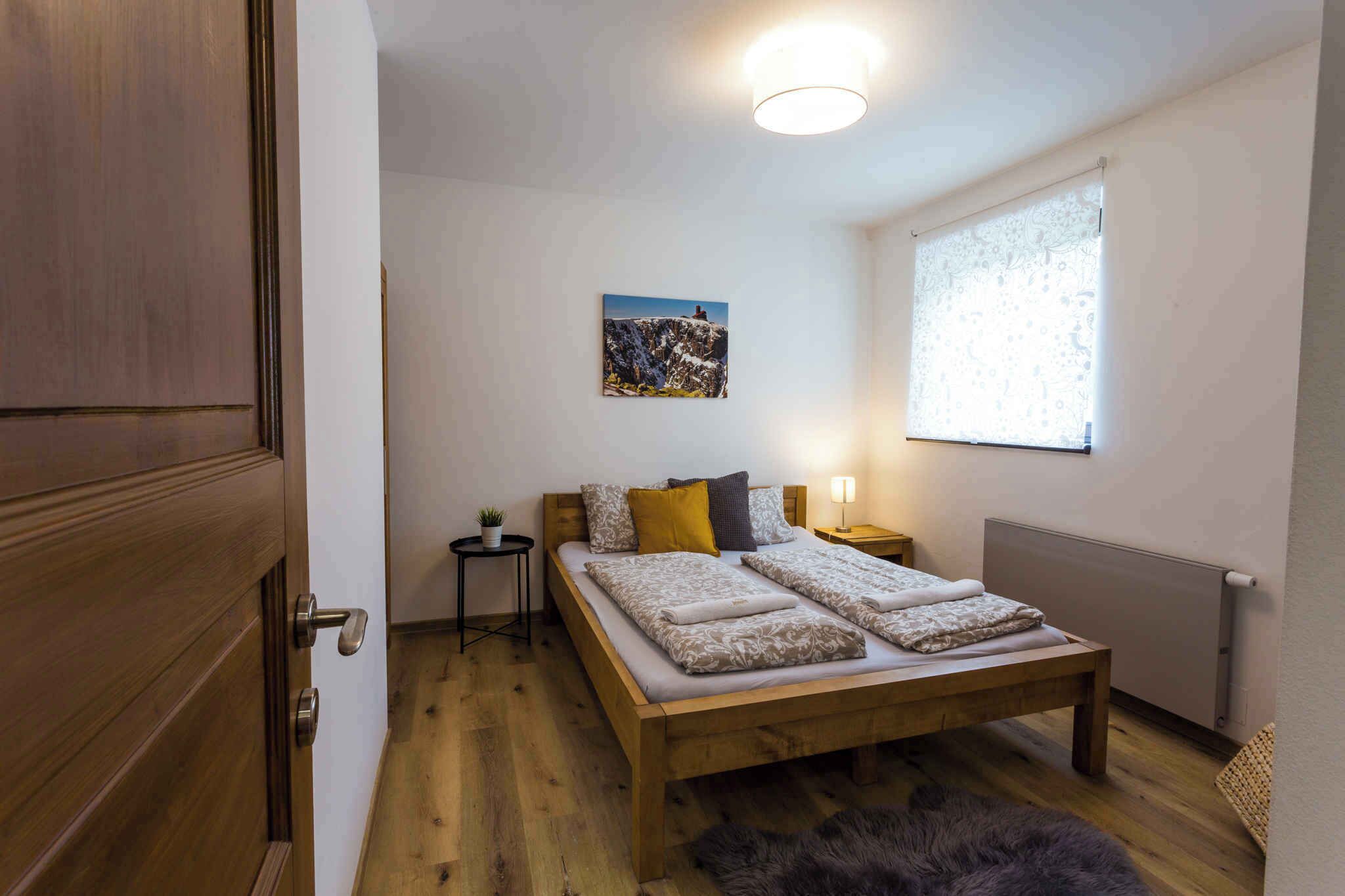 Ein Schlafzimmer mit einem hölzernen Bett, einem kleinen Nachttisch, einem Wandbild und einem Heizkörper.