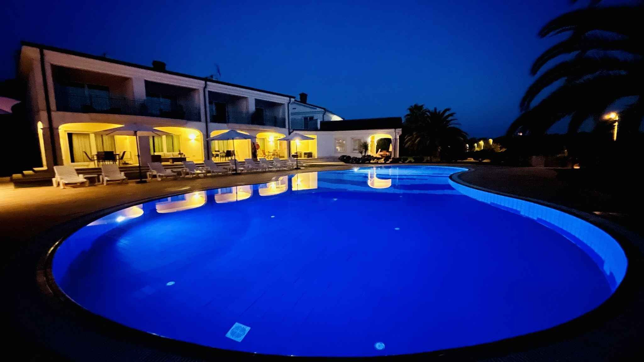 A swimming pool with a blue tint, surrounded by a building with multiple balconies and outdoor seating areas.