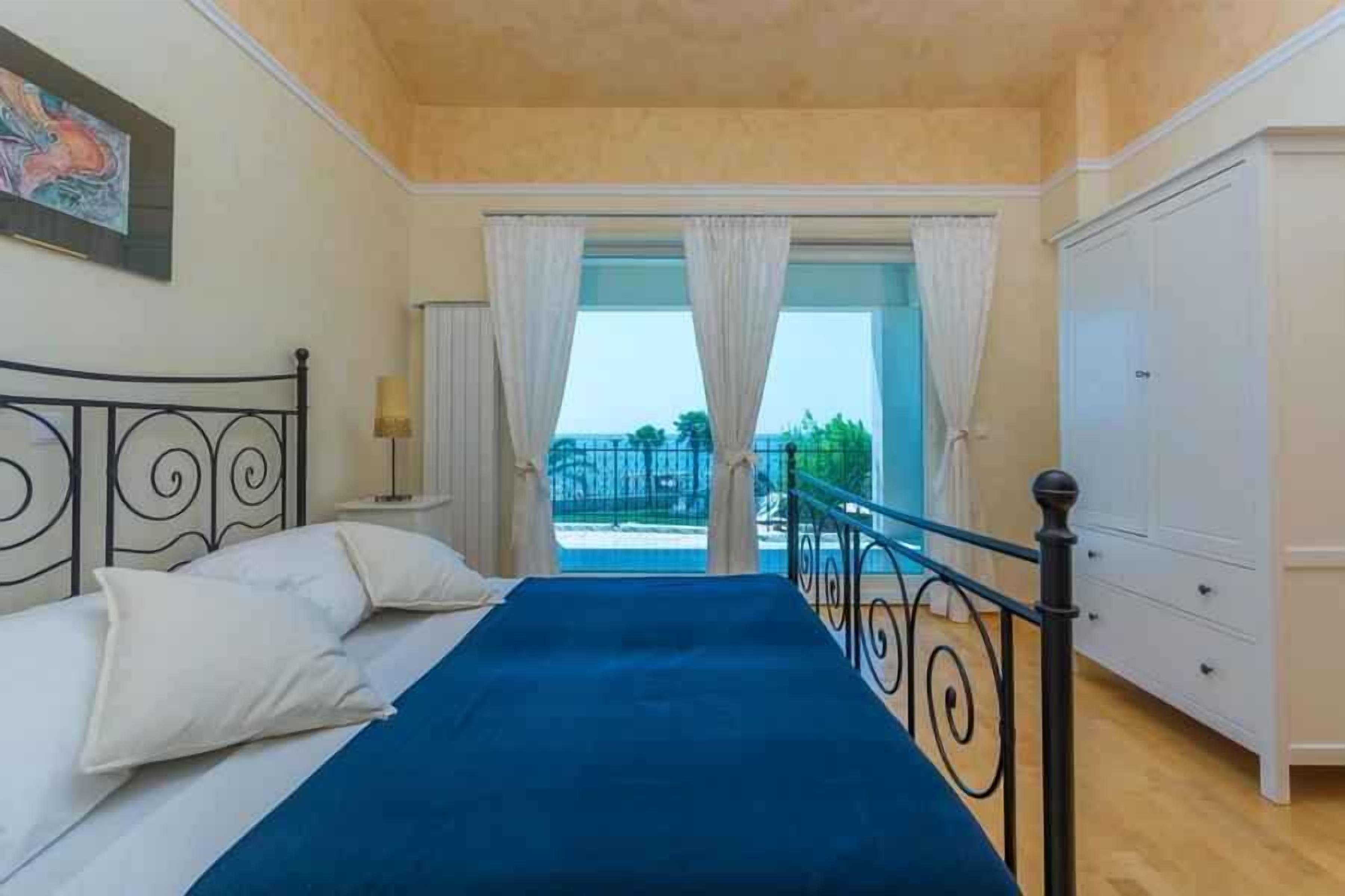 A bedroom with a bed, curtains, a nightstand, a lamp, a wardrobe, and a balcony with a railing.