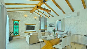 A modern living room with a large TV, a dining area with a glass table, and a kitchen in the background. - Villa with air conditioning and pool (Nova Vas/Novigrad)
