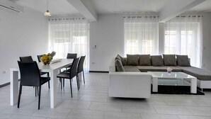 Un salon moderne avec un canapé blanc, une table basse en verre et un coin repas comprenant une table blanche et des chaises noires.