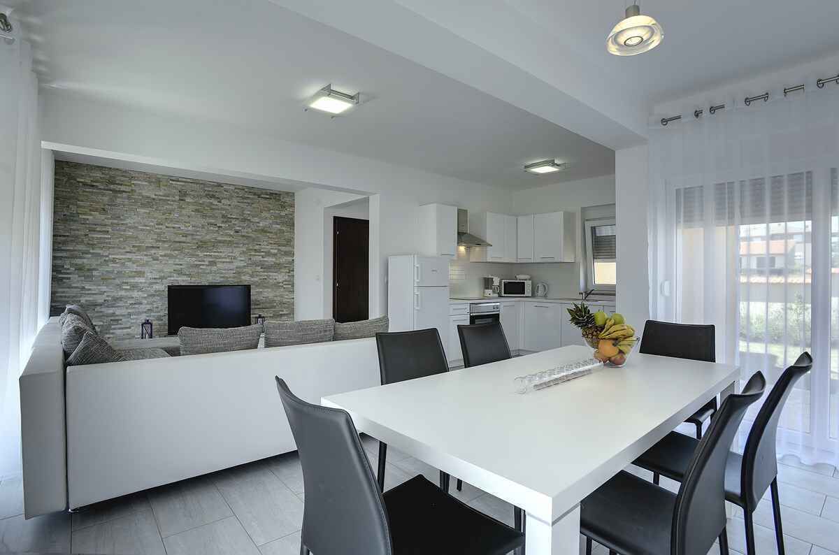 A modern kitchen with white cabinets, a built-in oven, and a flat-screen TV.