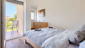 Une chambre à coucher comprenant un lit, une table de chevet, une fenêtre, un tableau et une porte coulissante donnant sur un espace extérieur.