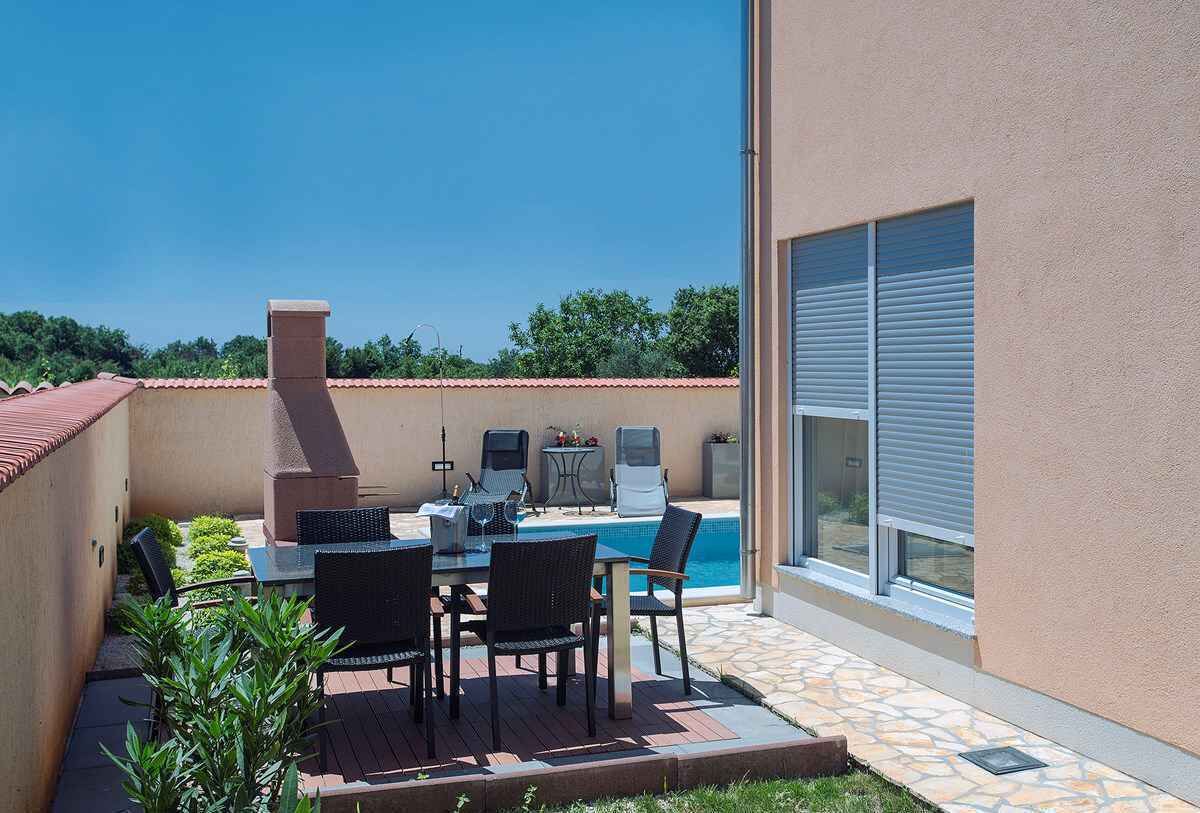 An outdoor patio with a pool, a barbecue grill, and a table with chairs.