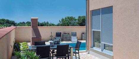 An outdoor patio with a pool, a barbecue grill, and a table with chairs.