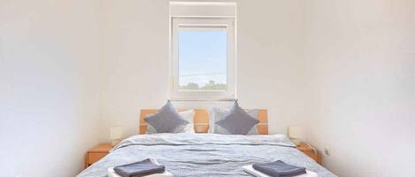 Une chambre à coucher avec un lit, des oreillers, une table de chevet, une lampe et une fenêtre donnant sur un beau paysage.