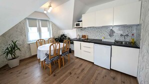 Uma cozinha compacta com armários brancos, bancada preta e um espaço de refeições com cadeiras de madeira.