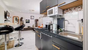 A modern kitchen with black cabinets, a microwave, a sink, and a bar area with stools. - Holiday apartment with large rooftop terrace and panoramic view (Bribir)