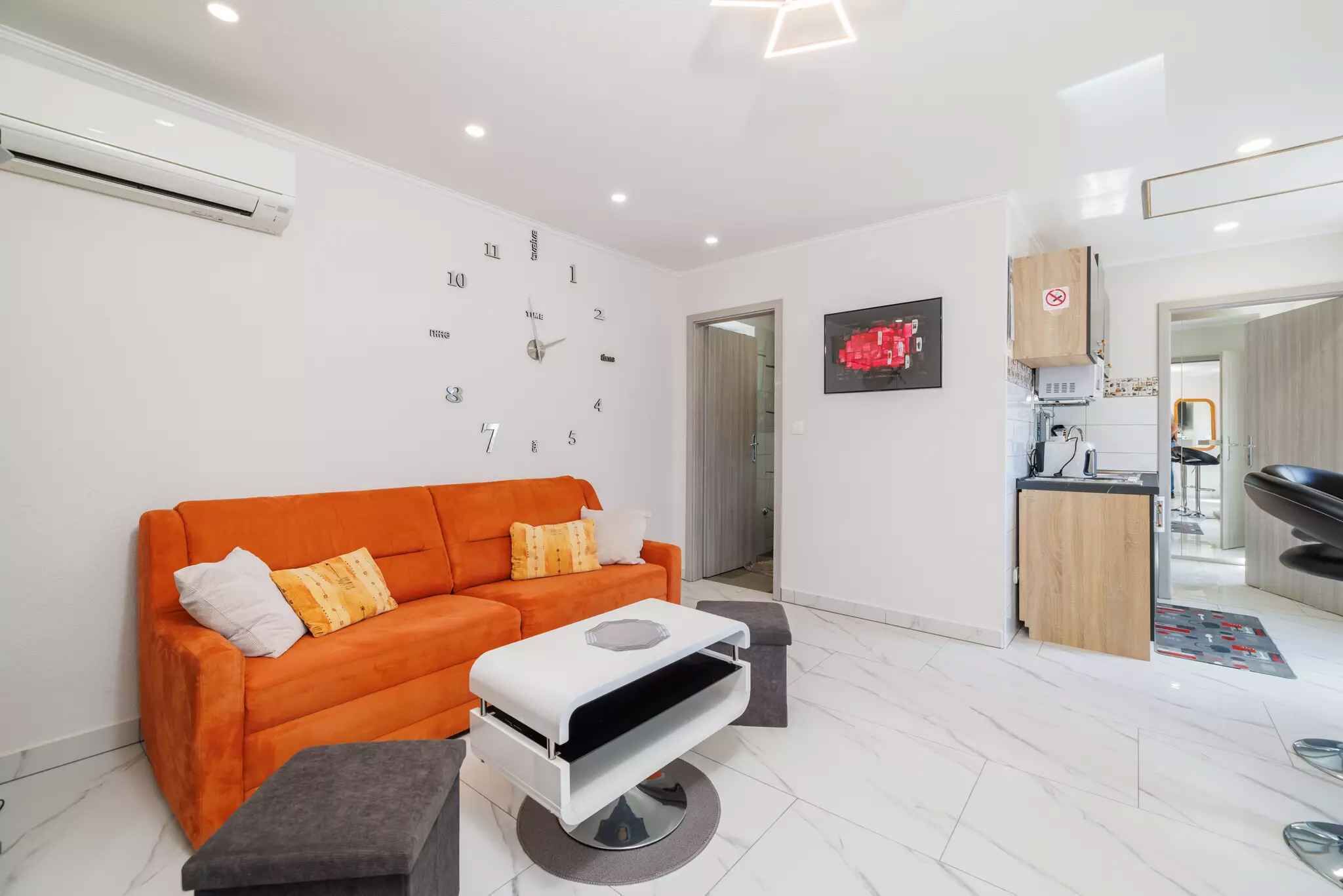 Un salon moderne avec un canapé, une table basse et un coin cuisine visible à travers une porte ouverte.