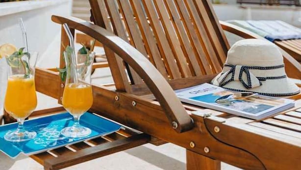 A wooden lounge chair with a magazine and a hat on it, and two glasses of orange juice on a tray. - Holiday home with outdoor pool, air conditioning and sea view (Punat)