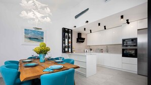 A modern kitchen with white cabinets, a central island, and a dining area with blue chairs and a wooden table. - Holiday home with outdoor pool, air conditioning and sea view (Punat)