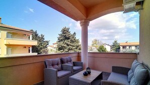 A covered outdoor seating area with wicker furniture and a table, overlooking a residential neighborhood.