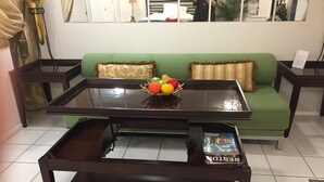 A living room with a glass-top coffee table, a magazine, and a fruit bowl.