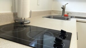 A kitchen with a black induction cooktop, a stainless steel sink, and a paper towel holder.