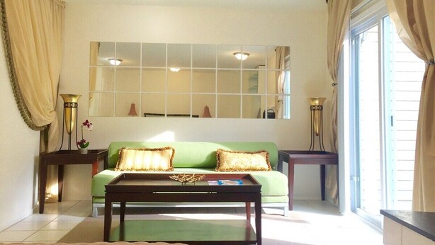 A living room with a green sofa, two side tables, a coffee table, and a large mirror on the wall.