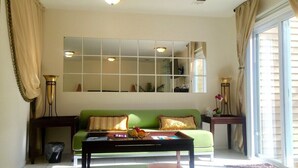 A living room with a green sofa, a coffee table with fruit, a large mirror, and a sliding glass door.
