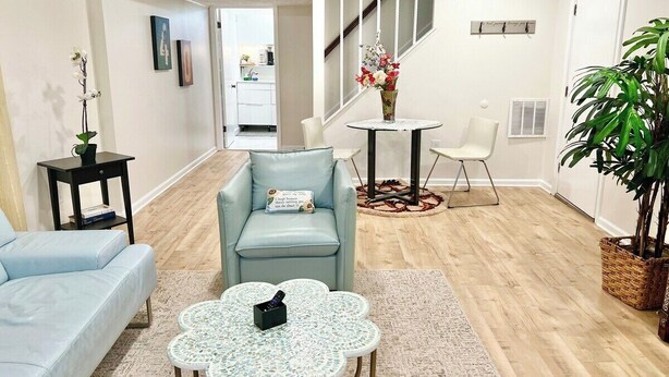Ein modernes Wohnzimmer mit einem hellblauen Sofa, einem runden Couchtisch, einem hellblauen Sessel und einem kleinen Tisch mit einem Blumenstrauß.