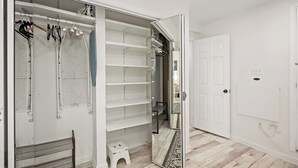 Um closet espaçoso com prateleiras abertas, cabideiro e um pequeno banco.