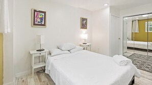 Quarto de hotel com cama, mesas de cabeceira, uma luminária e duas imagens emolduradas na parede.