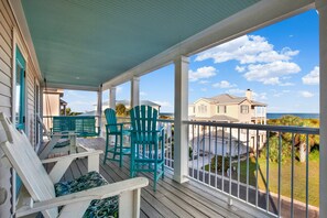 A covered porch with wooden chairs and a table, overlooking a residential area and the ocean. - Seconds to the Sea, Ocean views, Heated Pool Access (Tybee Island)