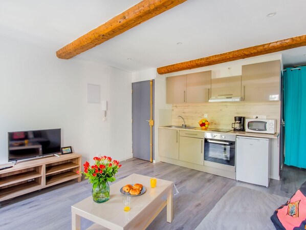 A compact living space with a kitchenette, a dining area with a table and chairs, a TV, and a vase with flowers. - Studio Bazeilles by Interhome (Toulon)