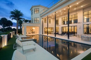 Een modern huis met een groot zwembad, buitenzitplaatsen en een goed verlicht interieur.