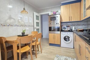 A modern kitchen with wooden cabinets, a built-in oven, microwave, and a washing machine.