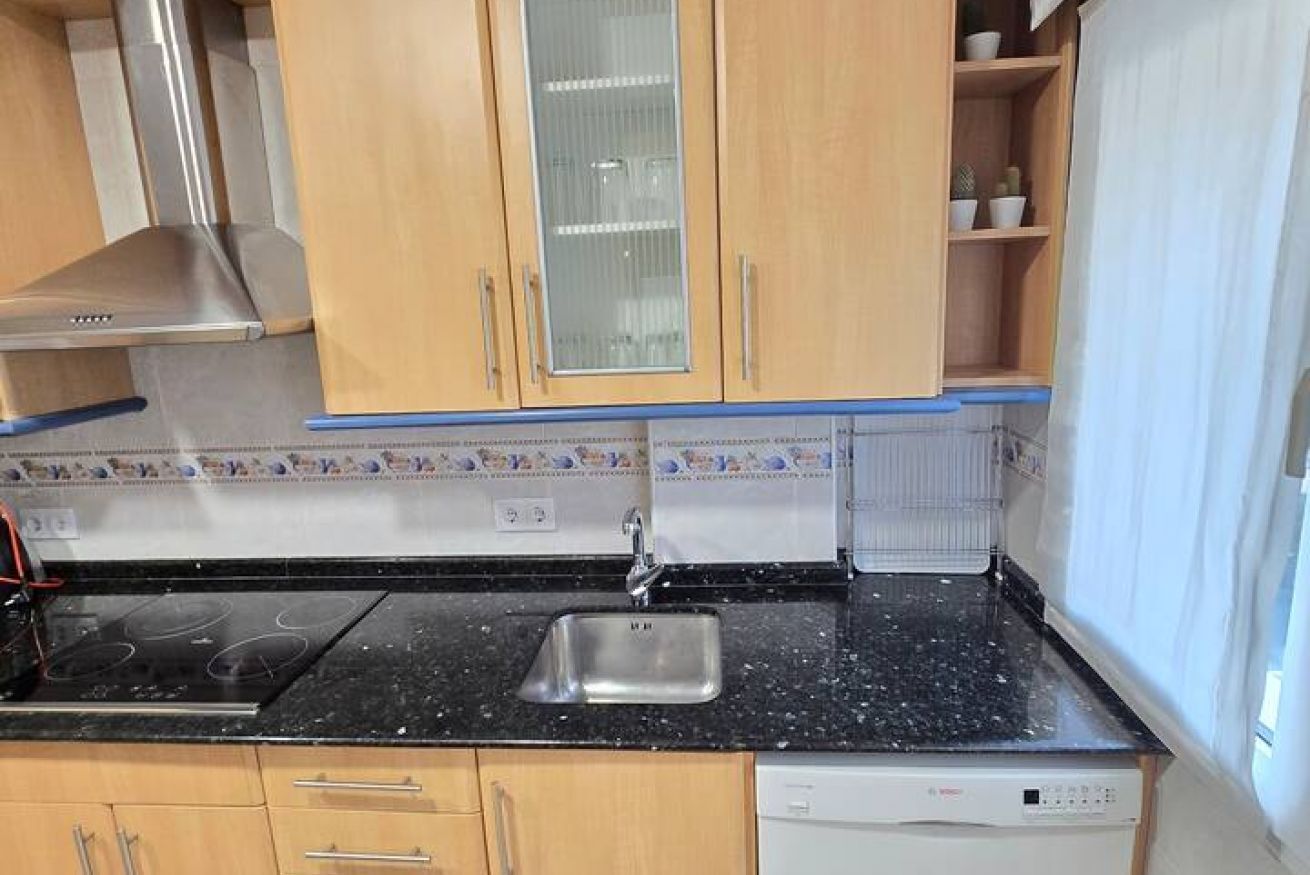 Cocina con armarios de madera, un lavamanos de acero inoxidable y una encimera negra.