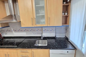 Cocina con armarios de madera, un lavamanos de acero inoxidable y una encimera negra.