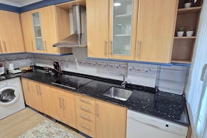 Una cocina con armarios de madera, una encimera negra, un lavamanos de acero inoxidable y una lavadora.