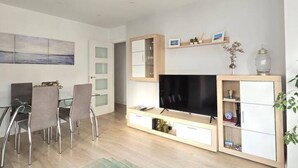Un soggiorno moderno con una TV a schermo piatto, un'area pranzo con sedie e una libreria.