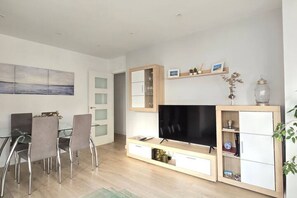 Una sala moderna con televisor de pantalla plana, un comedor con sillas y una estantería.