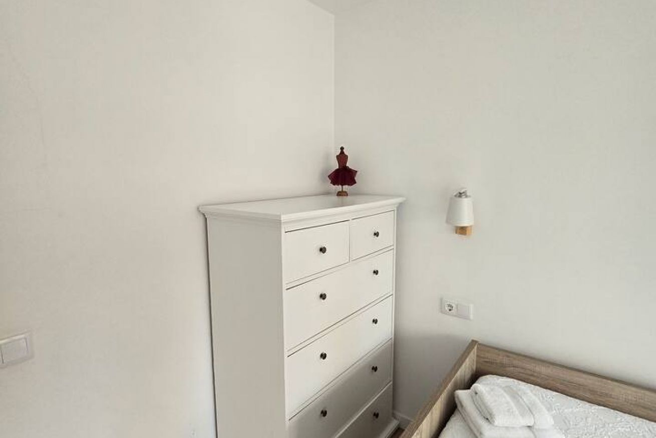 A white dresser with drawers, a small red object on top, and a wall-mounted light fixture.